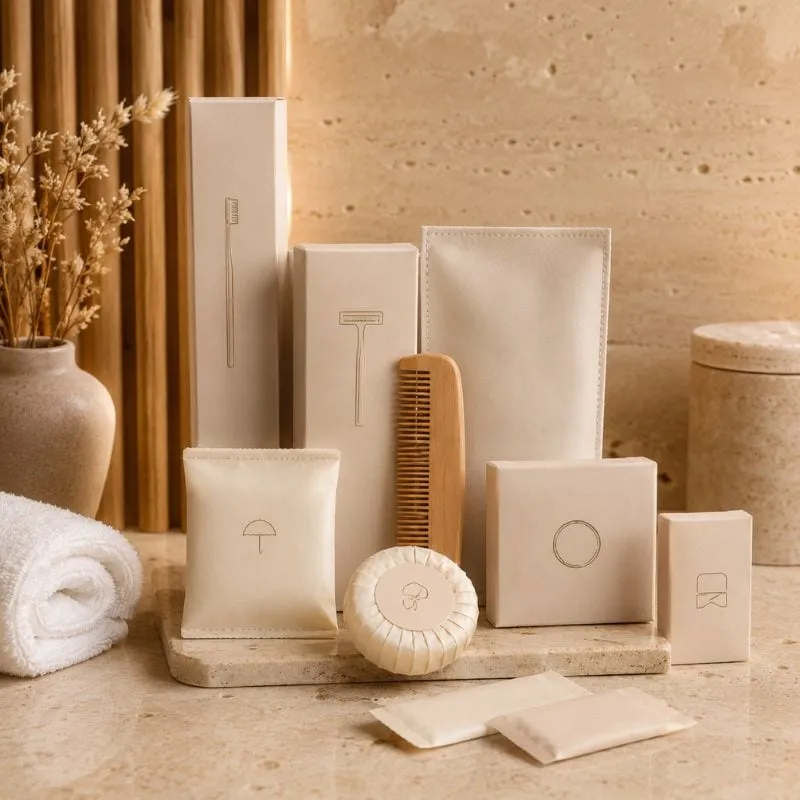Hotel amenity kits by UMYAN — cream card boxes with embossed icons, wooden comb and pleated soap on travertine